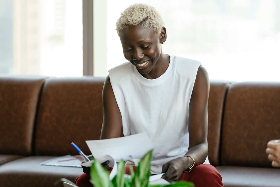 Femme noire souriante vérifiant un contrat sur un canapé en cuir